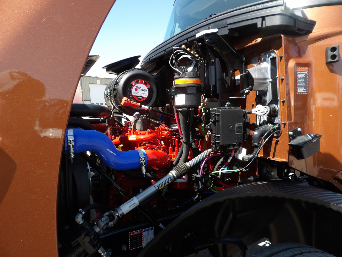 Mack MD7 engine bay showing blue coolant hose, red engine components, black hoses, wiring, and orange truck body.