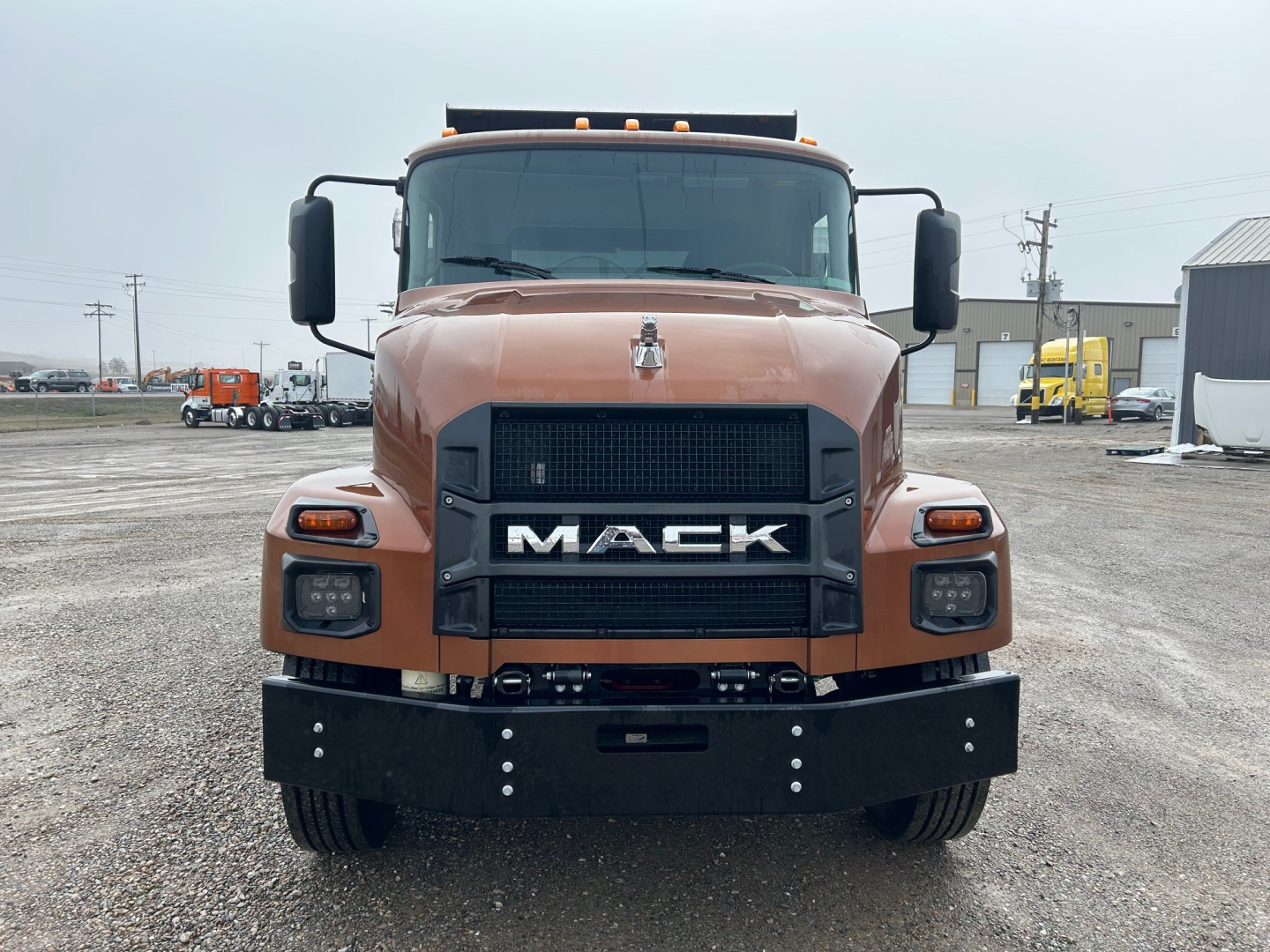 Front view of a brown 2026 Mack MD7 dump truck showing large black grille with MACK letters, headlights, and front bumper.