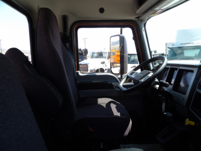 Cab interior of a 2026 Mack MD7 dump truck showing driver seat, steering wheel, dashboard, and side window with other trucks visible outside.