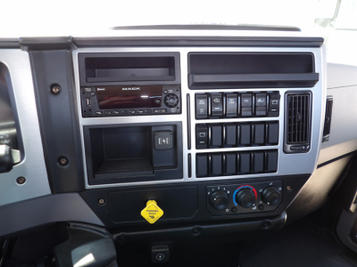 Mack MD7 dashboard and center console showing radio, climate controls, and numerous switches; yellow hood release label visible; dark gray/black plastic trim.