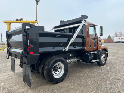 Dump truck rear-left view showing cargo bed and side mirrors, Mack MD7 chassis, with black steel dump body and dual rear wheels.