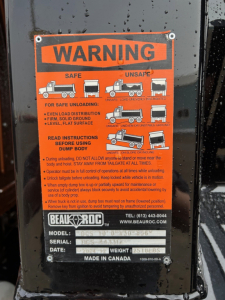 Warning label on Mack MD7 dump truck component showing safe unloading instructions and pictograms.