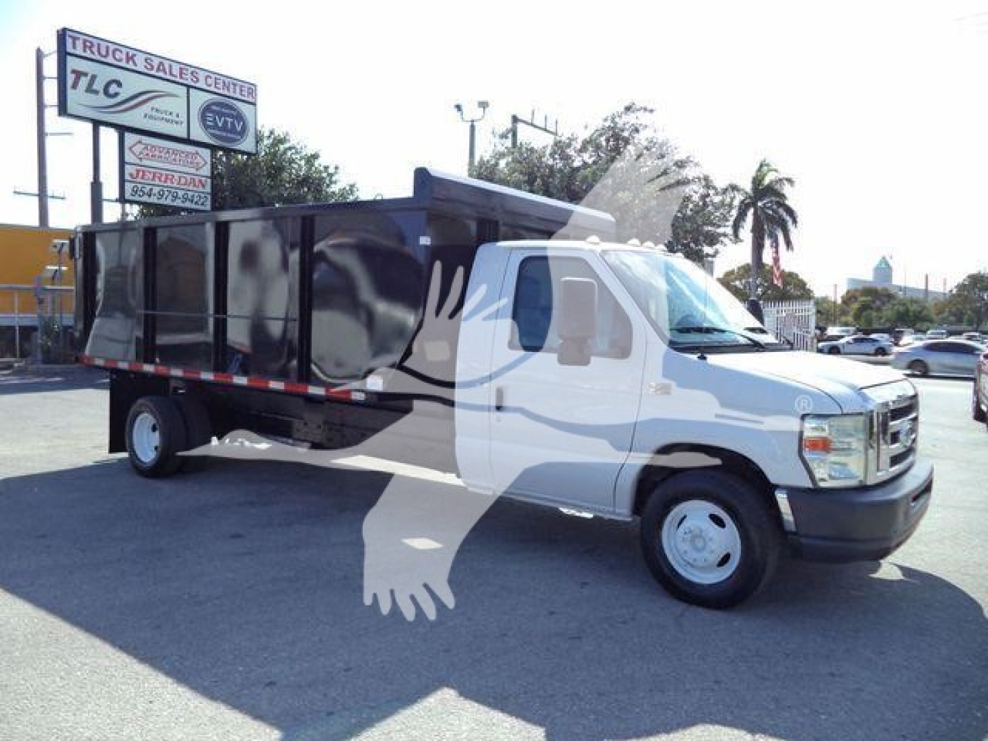 Dump truck body with black dump bed attached to white Ford E-450 cab, side profile view. Signage on lot in background reads ‘TRUCK SALES CENTER TLC’ with a palm tree visible.