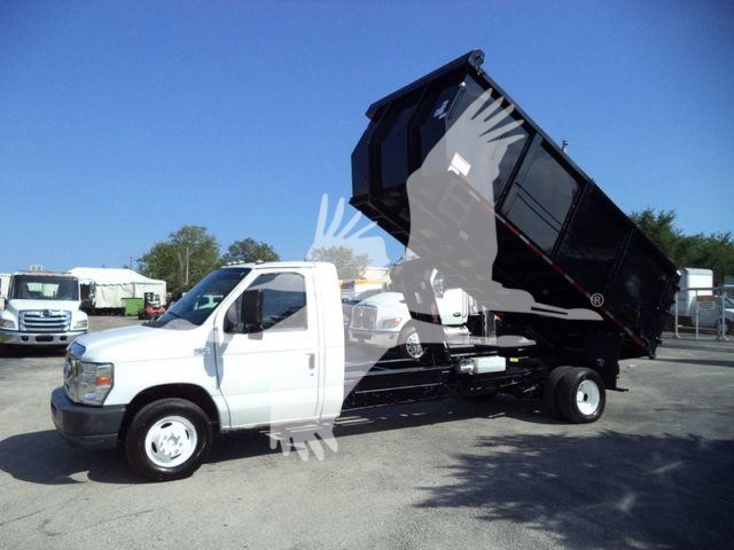 Ford E450 dump truck with tilting black dump bed raised, white cab, side view showing hydraulics and dump mechanism.