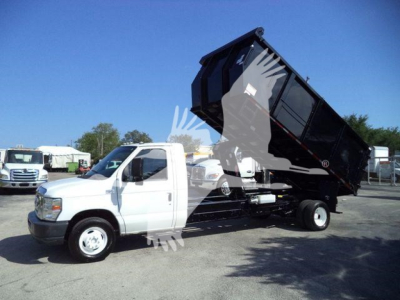 Ford E450 dump truck with tilting black dump bed raised, white cab, side view showing hydraulics and dump mechanism.