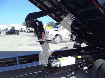 Ford E-450 dump truck chassis showing hydraulic system with white reservoir and metal frame under open bed.