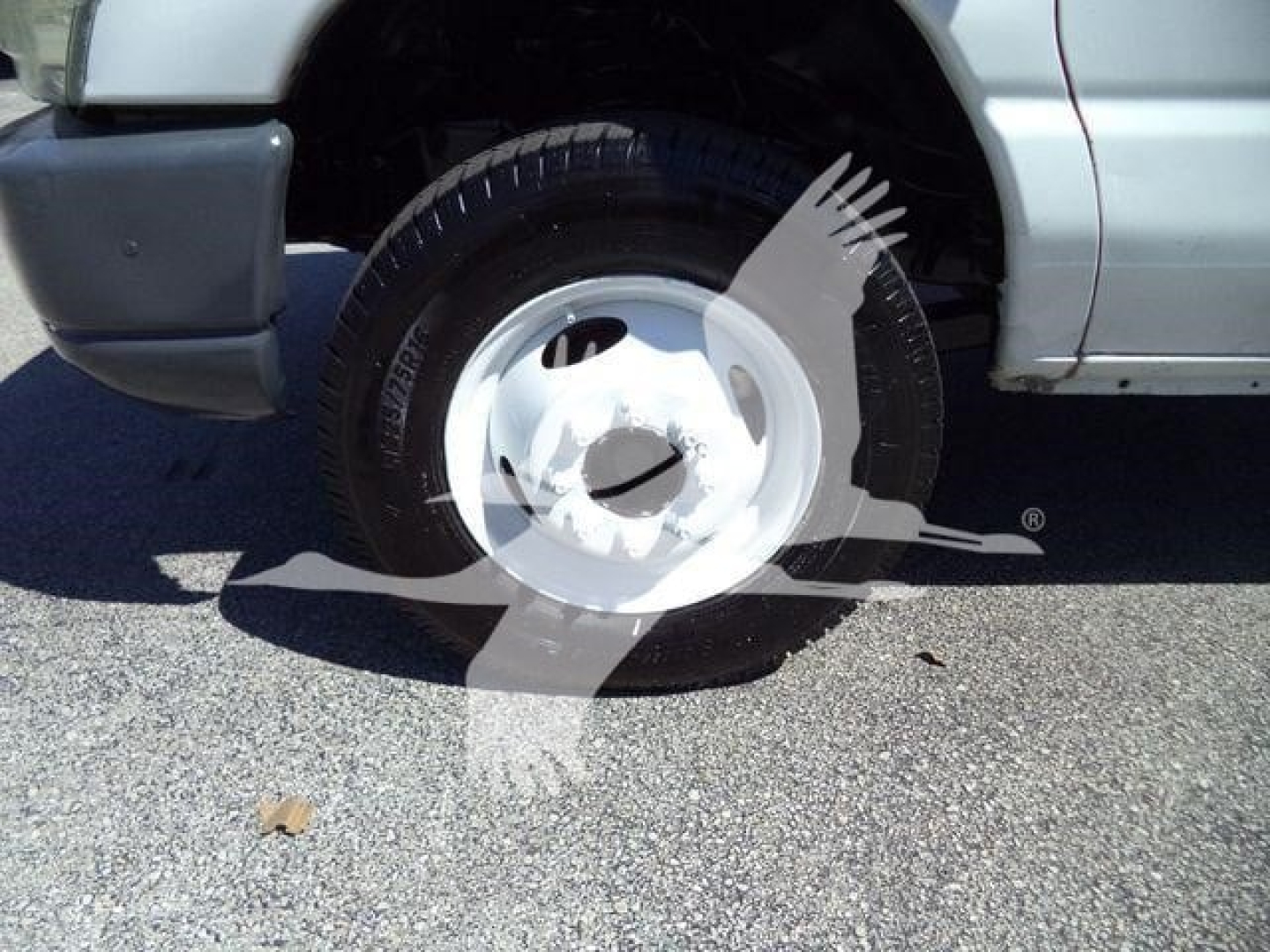 Ford E-450 front passenger side wheel well and tire showing wheel inside a box truck, partial front bumper, silver body paint.