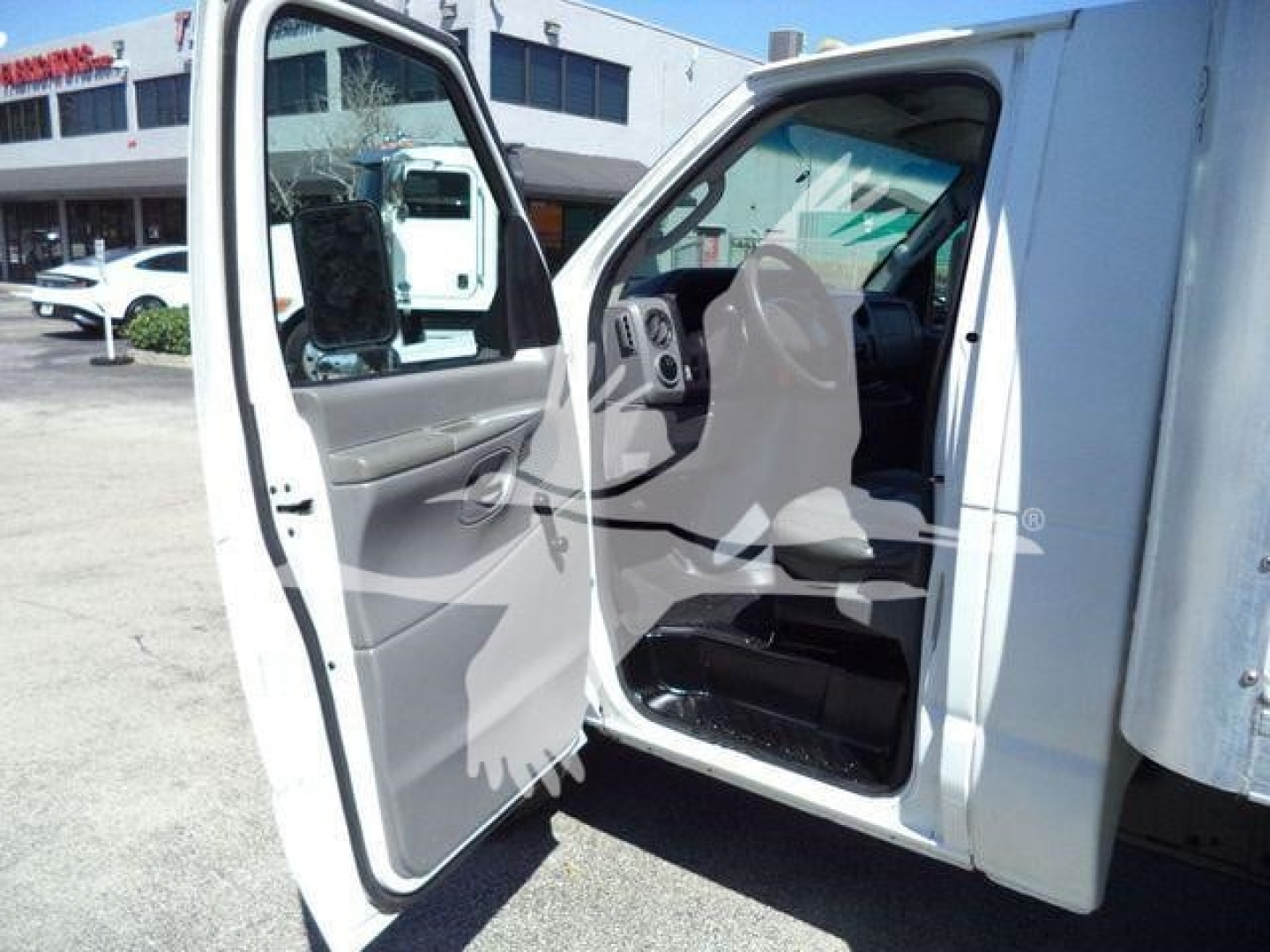 Ford E-450 van interior view with front door open showing gray dashboard and seats; exterior white body; part of box truck cargo area visible.