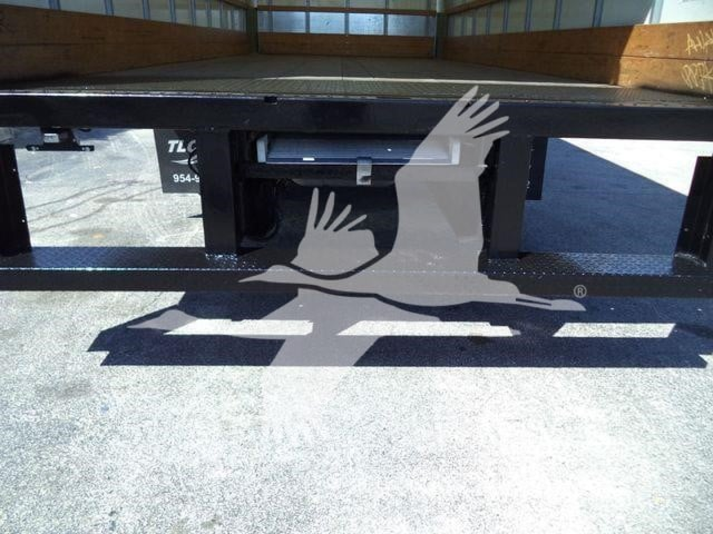 Truck bed bottom showing a black steel frame and shadow of a logo on the ground.