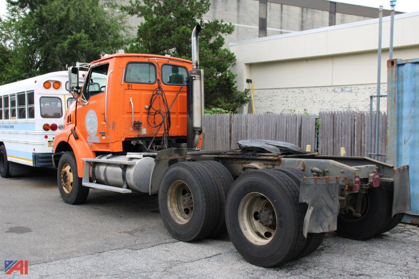 Orange 2005 Sterling LT9500 series tractor truck chassis with dual rear axles and a small school bus in background.