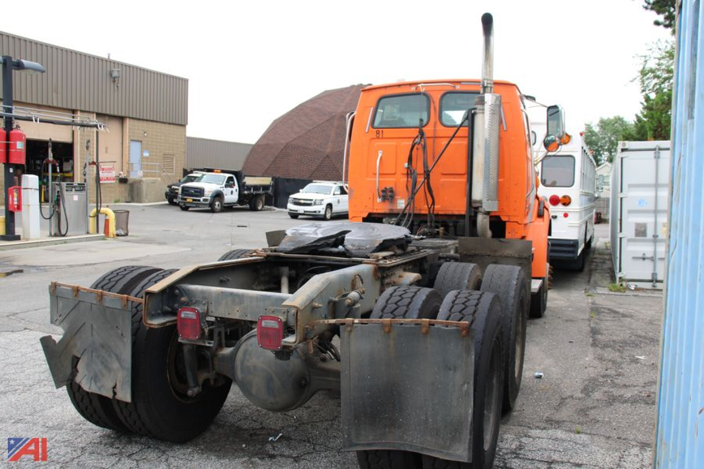 Tractor-trailer chassis with orange cab, rear view showing dual rear axles and fifth wheel mount.