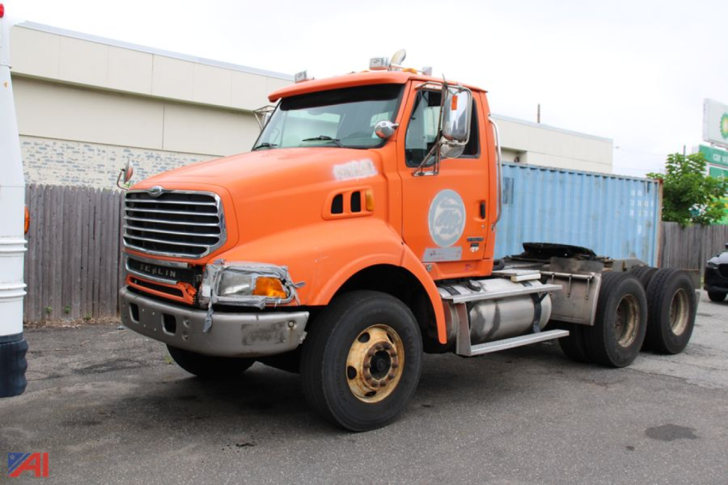 Orange Sterling LT9500 series tractor cab with logo on door, showing front grille, headlights, and dual rear axles; windshield and mirrors visible.