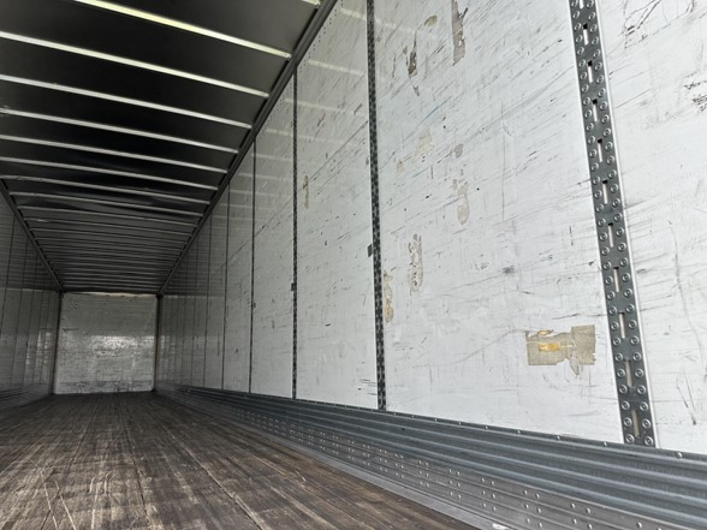 Trailer interior showing aluminum side walls with ribbed metal strips and wooden floor in a 53' Wabash dry van unit.