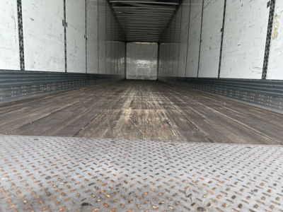 Inside view of empty 2022 Wabash Duraplate trailer with wooden floor and metal sidewalls, rear ramp open, trailer interior long and rectangular.