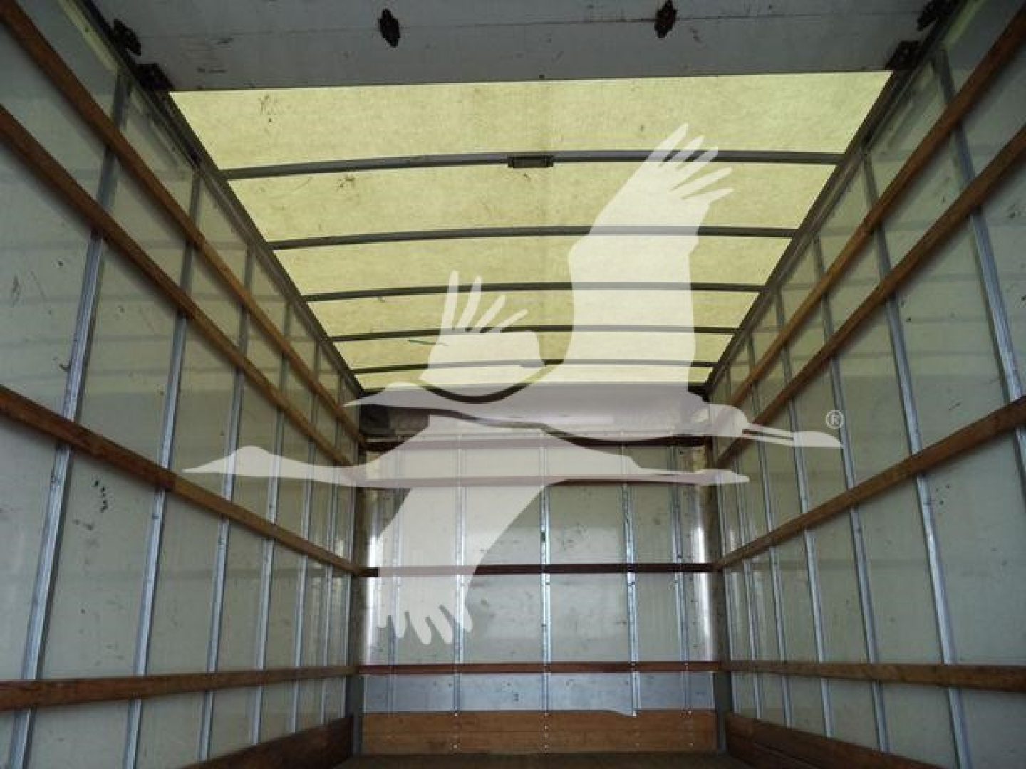 Inside view of a box truck cargo area showing metal walls and wooden stringers with light from rear doors.