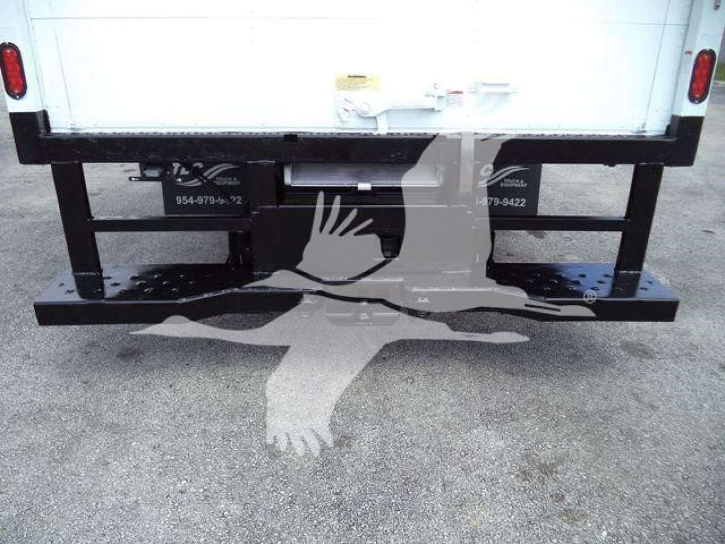 Ford E-450 rear view showing frame and bumper with hitch receiver and license plate lights, stock number decals, and a white box truck cargo area.
