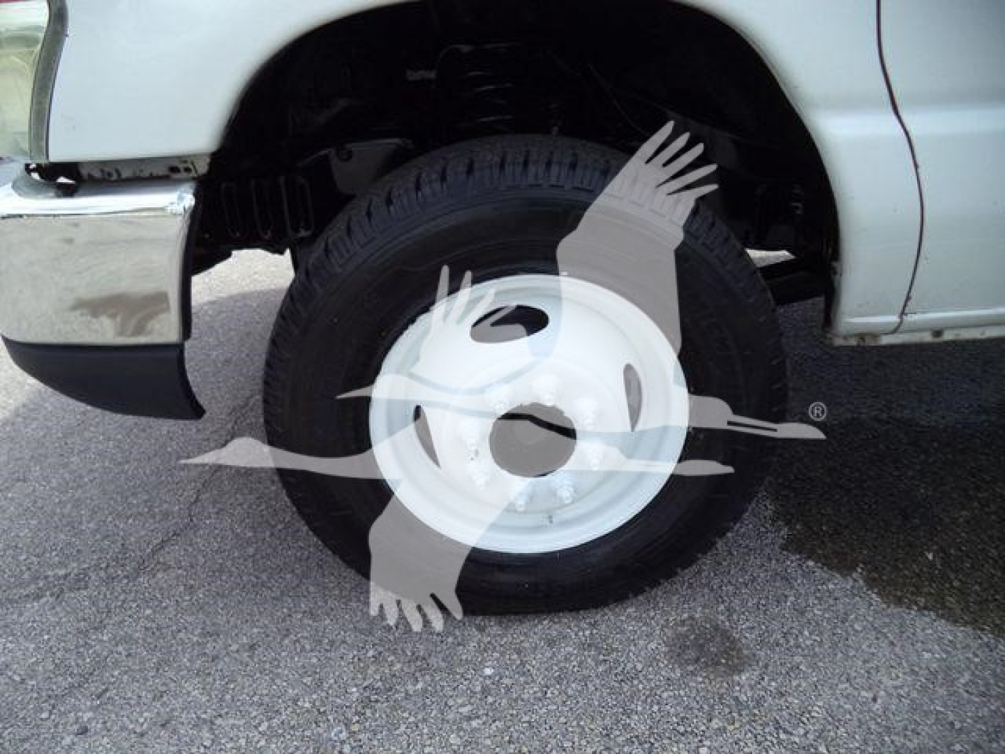 Ford E-450 wheel and front fender view showing steel white hubcap and tire in service condition.