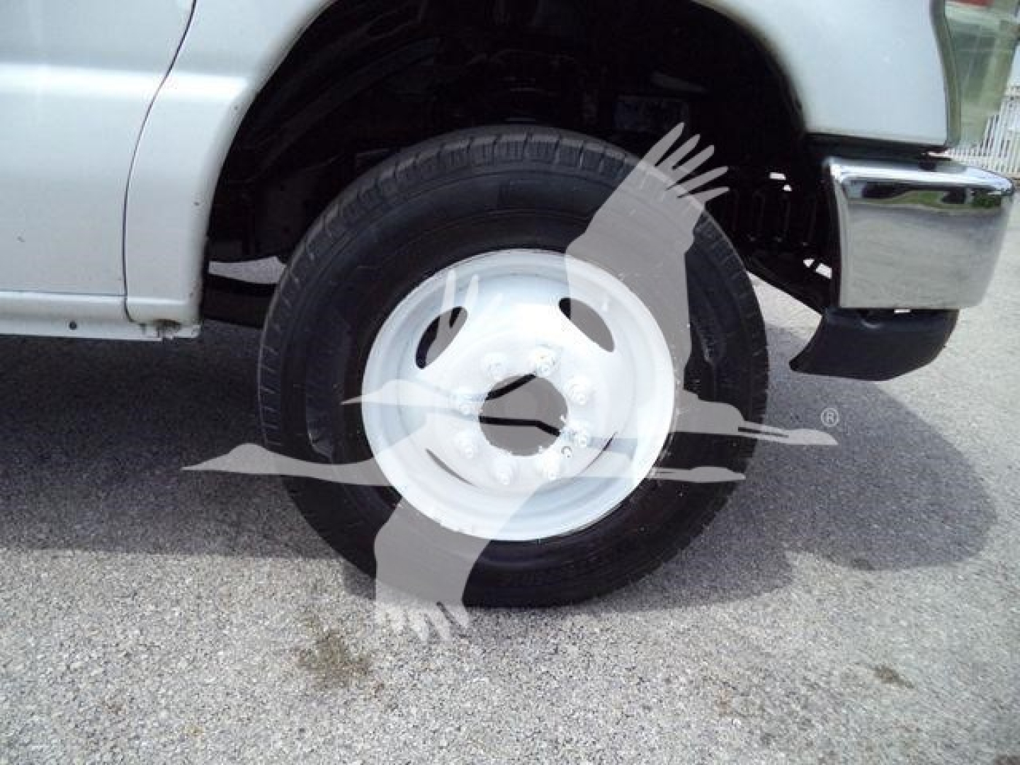 Wheel well and white steel wheel of a Ford E450 box truck showing tire and wheel hub and partial front bumper.