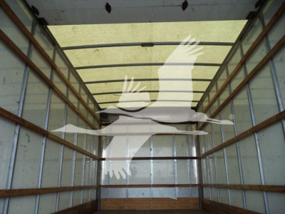 Inside view of a box truck cargo area showing metal walls and wooden stringers with light from rear doors.