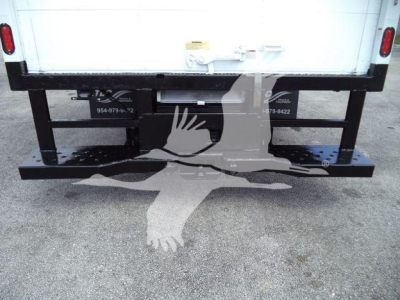 Ford E-450 rear view showing frame and bumper with hitch receiver and license plate lights, stock number decals, and a white box truck cargo area.