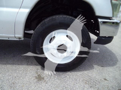 Wheel well and white steel wheel of a Ford E450 box truck showing tire and wheel hub and partial front bumper.