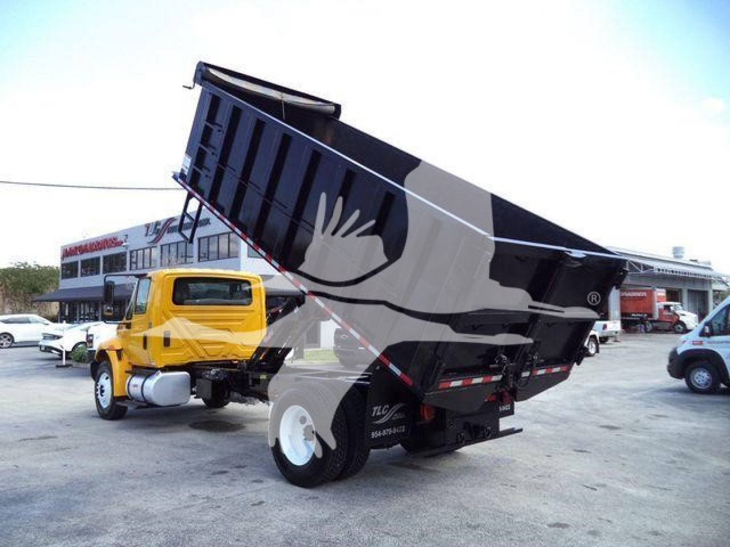 Dump truck on a dealership lot with a raised bed, 2019 International 4300, yellow cab, black dump body in service position.