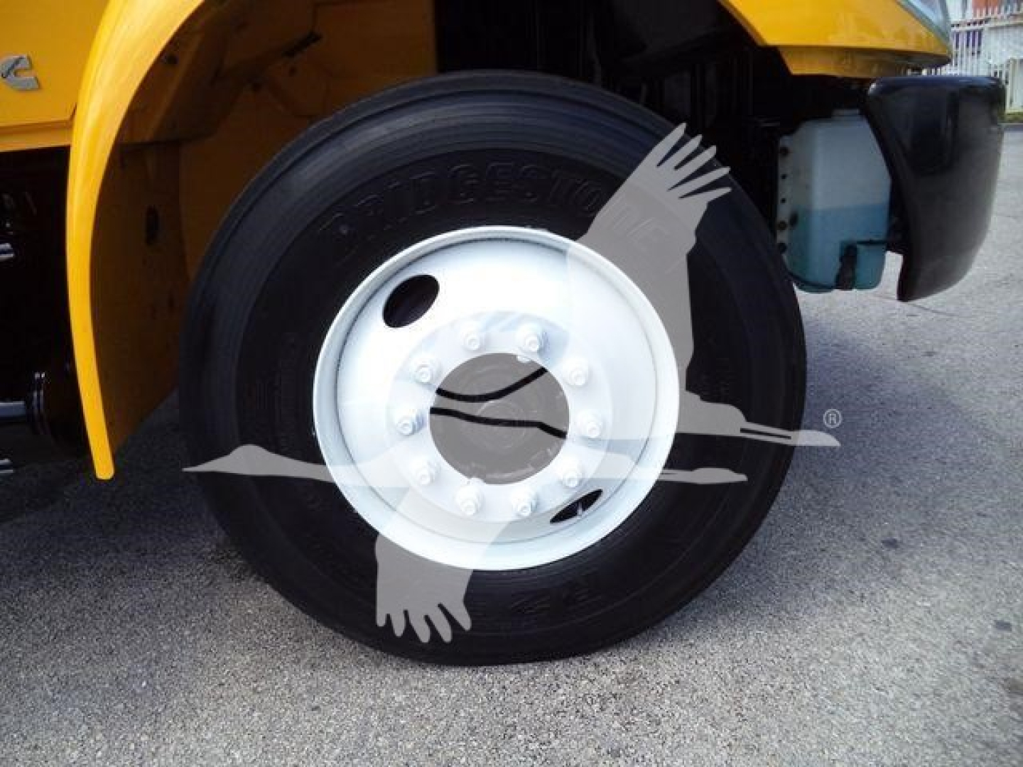 Truck wheel close-up showing steel white rim and tire with tread, partially visible yellow body and blue coolant reservoir.