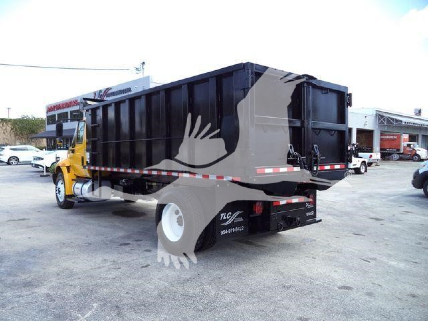 Truck bed of a 2019 International 4300 dump truck with black bed and yellow cab; visible text on side includes logo and contact numbers, rear lights, and reflective tape.