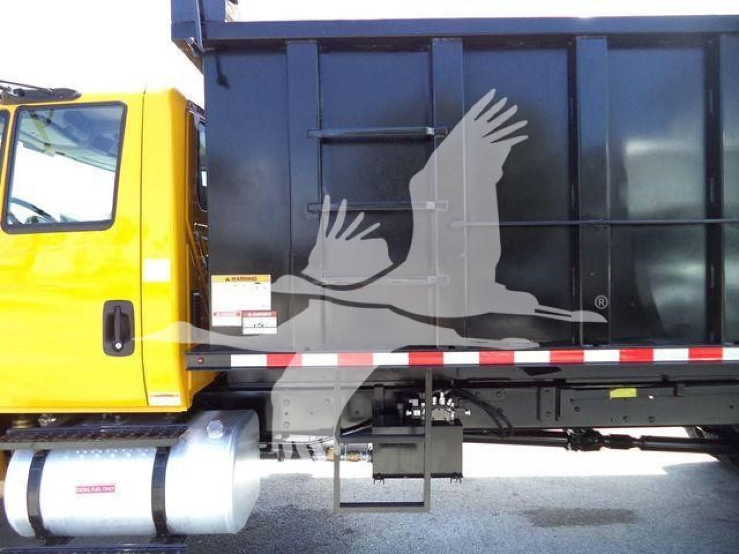 Truck side view showing a yellow truck cab attached to a black dump bed with a bird graphic decal and safety rails.