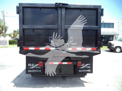 Dump truck bed rear view showing TLC logo and contact numbers, reflective tape, and tailgate latches.