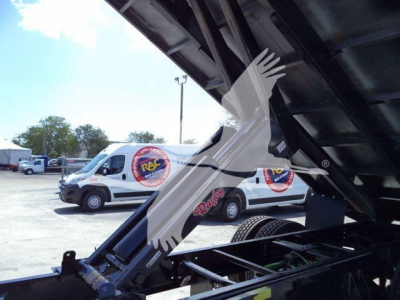 Truck engine bay with hood open and landscape truck lot in background; raised hood shows engine components; multiple white vans with circular logos visible.