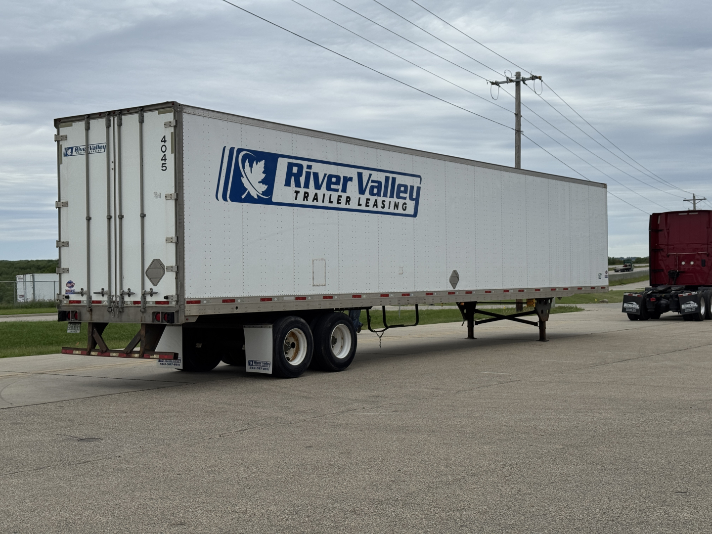 Trailer side view showing River Valley Trailer Leasing logo on a white utility trailer under a cloudy sky.