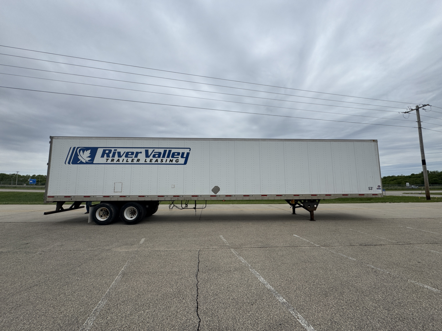 Trailer side view showing River Valley Trailers Leasing logo on a white utility trailer with dual rear axles and a ramp door.