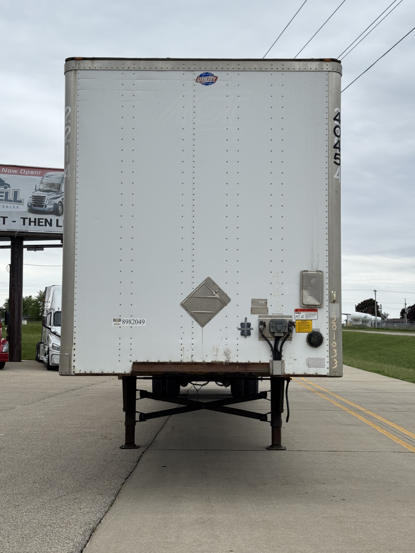 Trailer back view showing rear doors with diamond placard, electrical connections, and support legs under a Utility 4000Dx trailer.