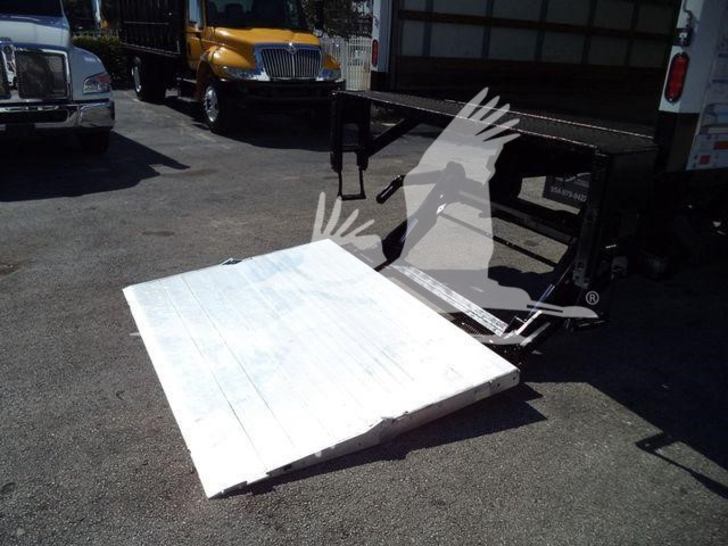 Flat white steel loading ramp in front of a truck bed, with a black tailgate frame and other carriers in the background.