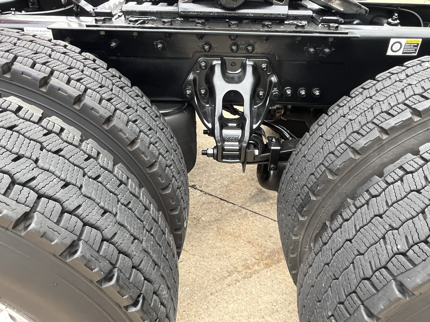 Kenworth T680 chassis view showing dual rear axles and suspension hanger; visible are tires, frame rails, and brake components.