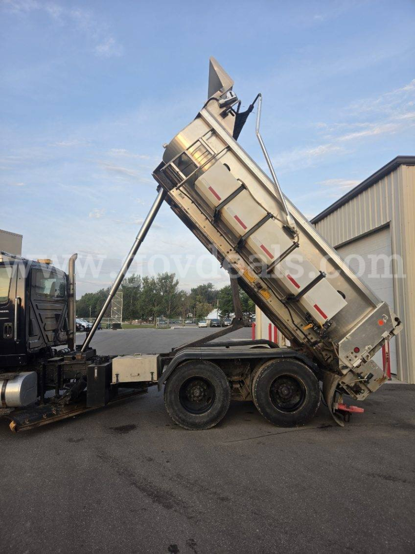 Truck dump bed tilted up on a semi trailer with a plow attachment in a yard.