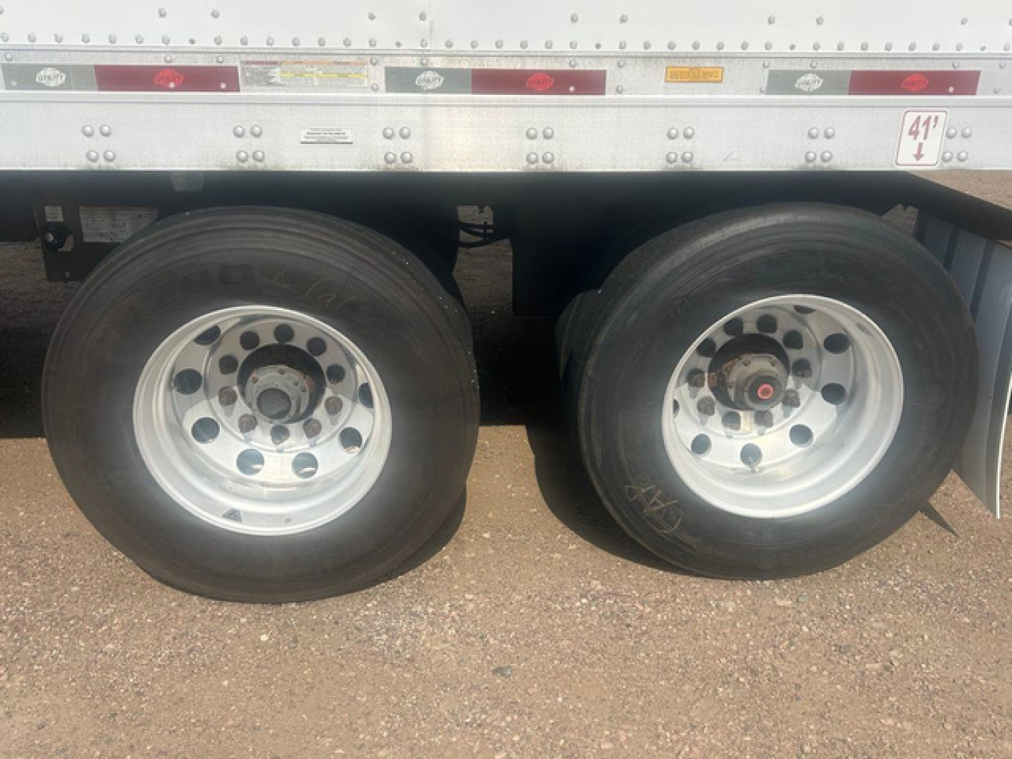Dual rear trailer wheels showing steel rims and tires under a utility trailer chassis.