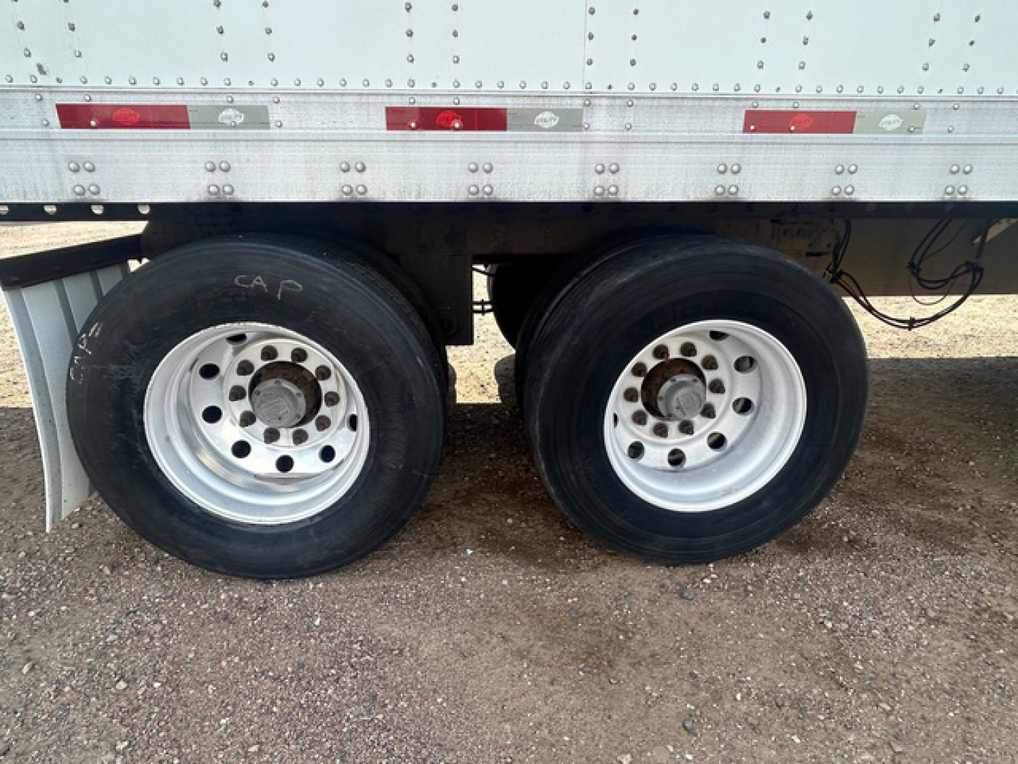 Dual rear trailer wheels with black tires and silver rims under a silver utility trailer side panel.