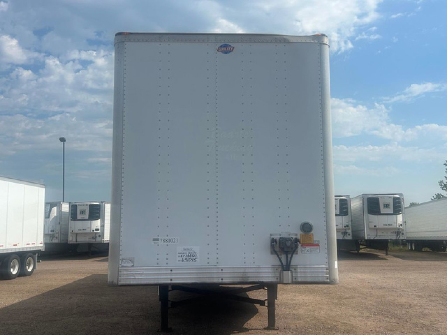 Trailer rear view showing plain aluminum box with riveted walls, rear lights, hitch, and landing gear. No visible text readable from image.
