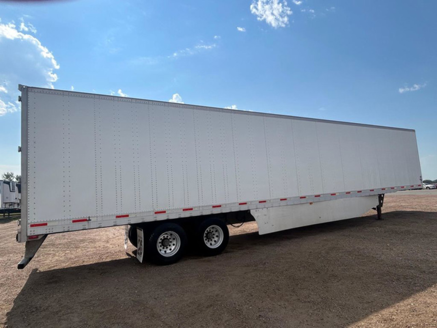 Trailer side view showing a white enclosed cargo trailer with dual rear axles and kingpin hitch.
