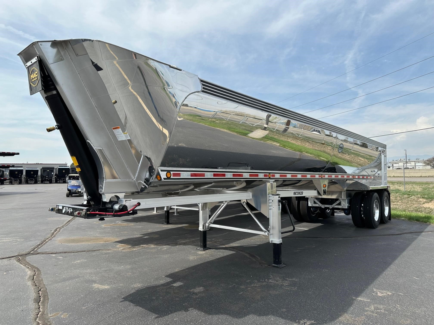 Trailer side view of a new Mac Macsimiser dump trailer with raised bed, dual rear axles, and landing legs extended.