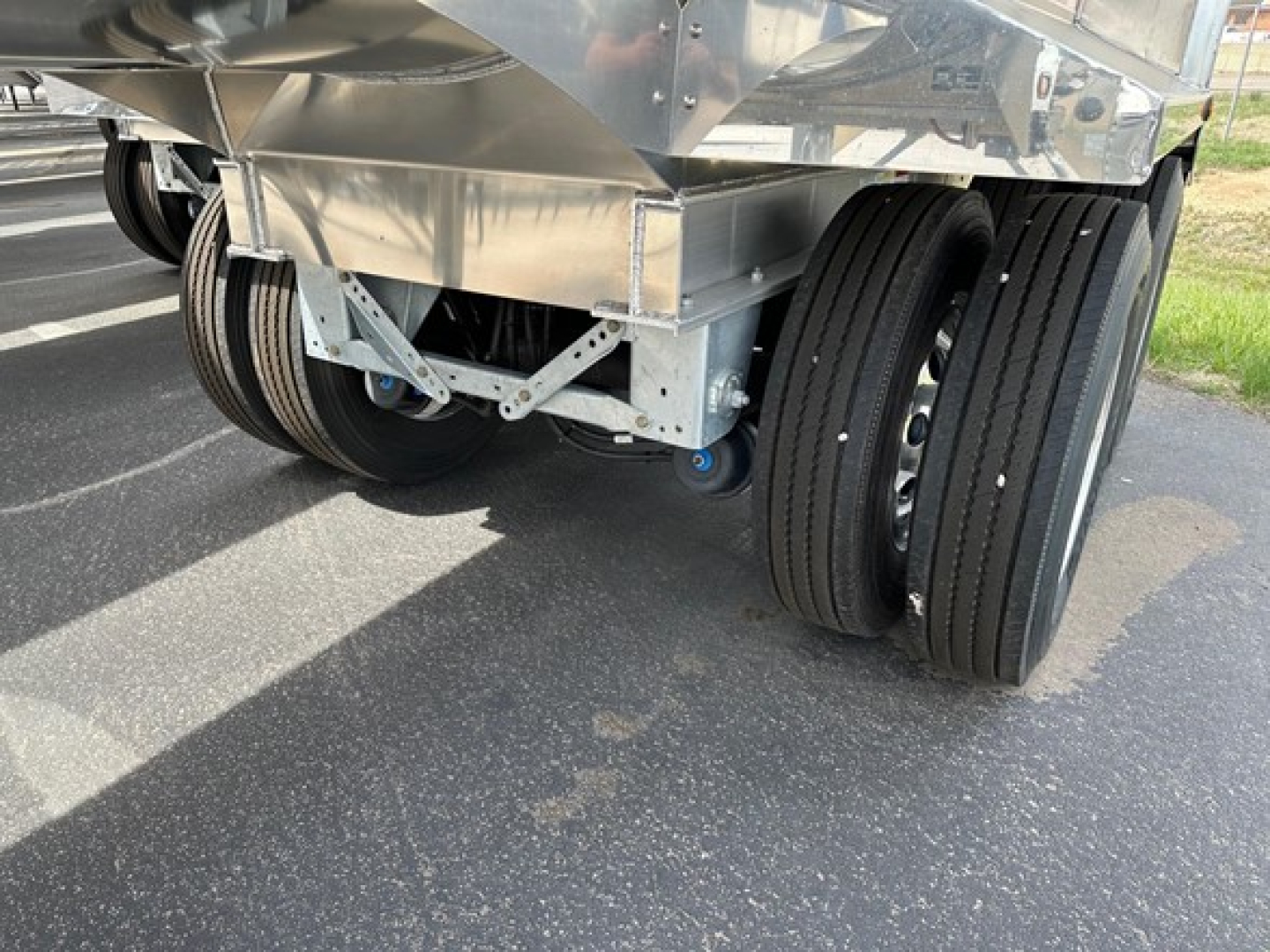 Trailer undercarriage showing dual rear axles with black tires and polished aluminum dump body edge, no visible text.