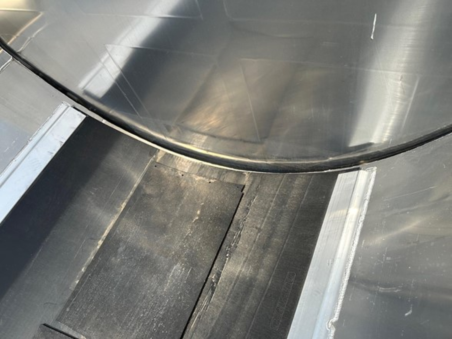 Circular metal end dump trough with curved lip and metal seams; shiny steel surface with welded joints.