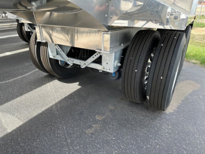 Trailer rear showing dual axles with heavy-duty aluminum end dump body, polished metallic finish, undercarriage and wheels visible.