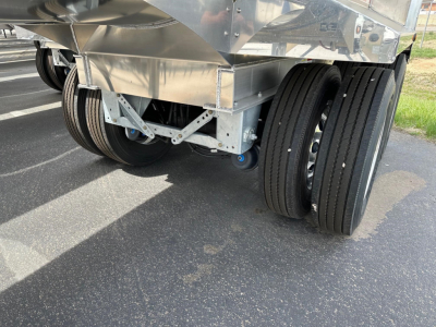 Trailer undercarriage with dual rear axles and polished metal body, multiple black tires, and support frame visible.