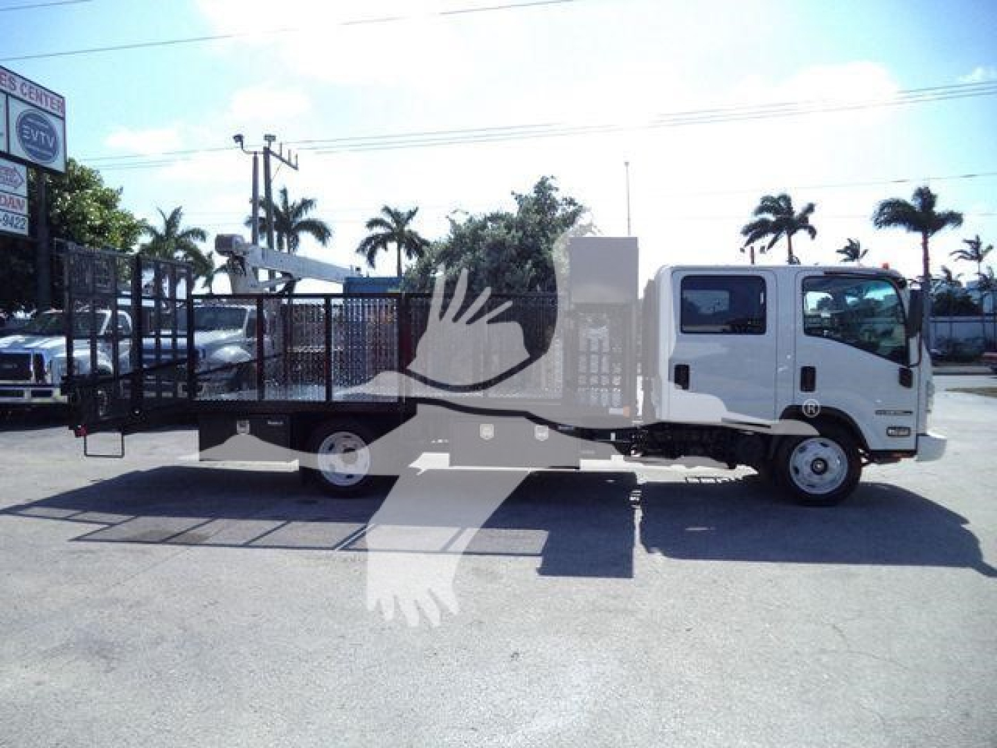 Isuzu NPR-HD cab and flatbed tow truck in a dealership lot with palm trees in background.