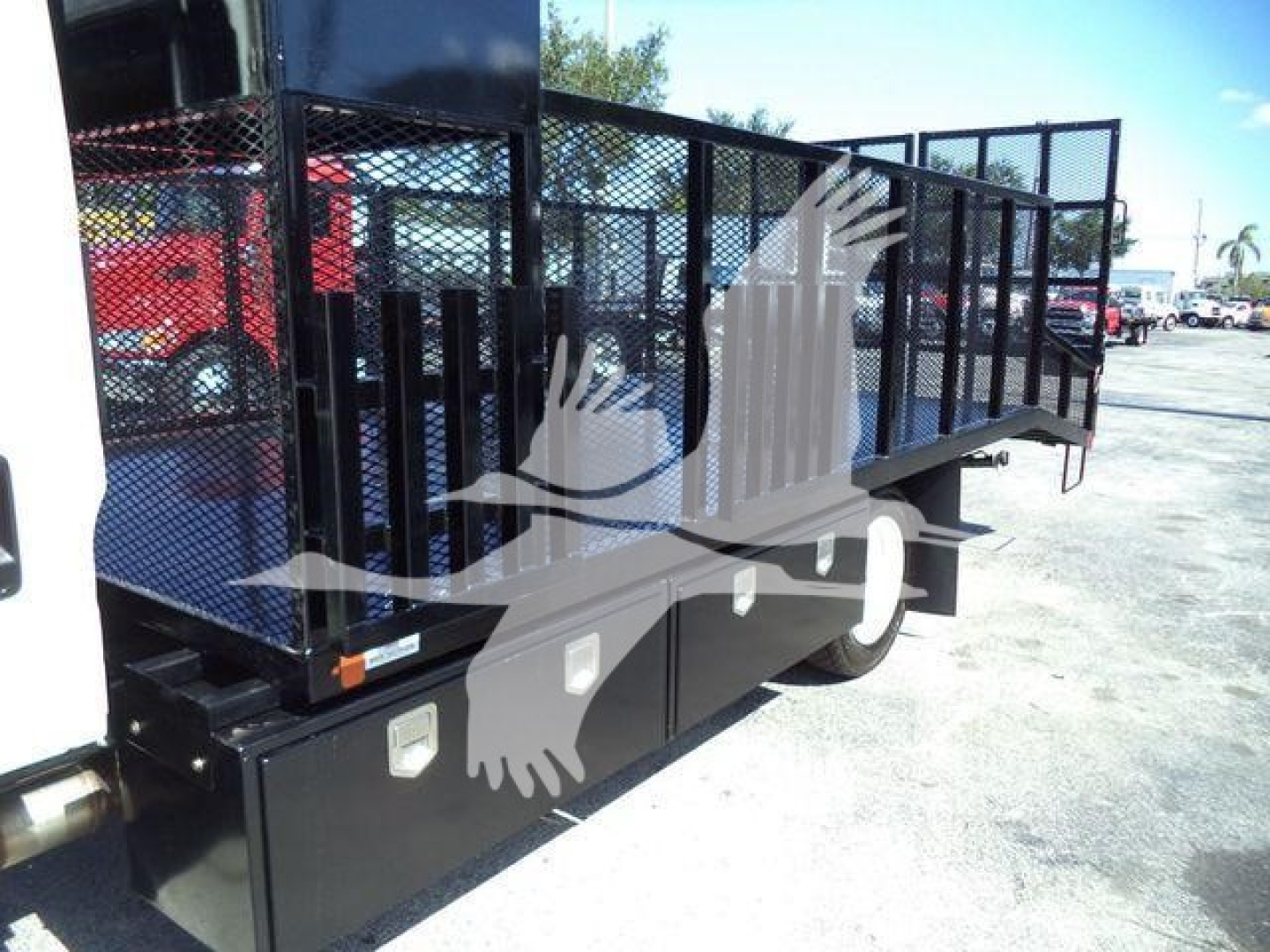 Isuzu NPR-HD flatbed truck side view showing black metal stake bed with storage boxes and railing.