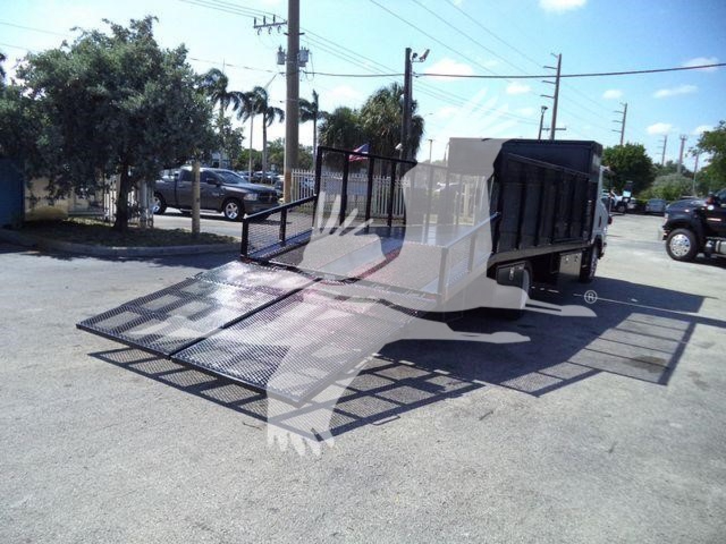 Isuzu NPR-HD truck equipped with a hydraulic ramp lift in a dealership lot, side view showing ramped bed and rear cargo area.
