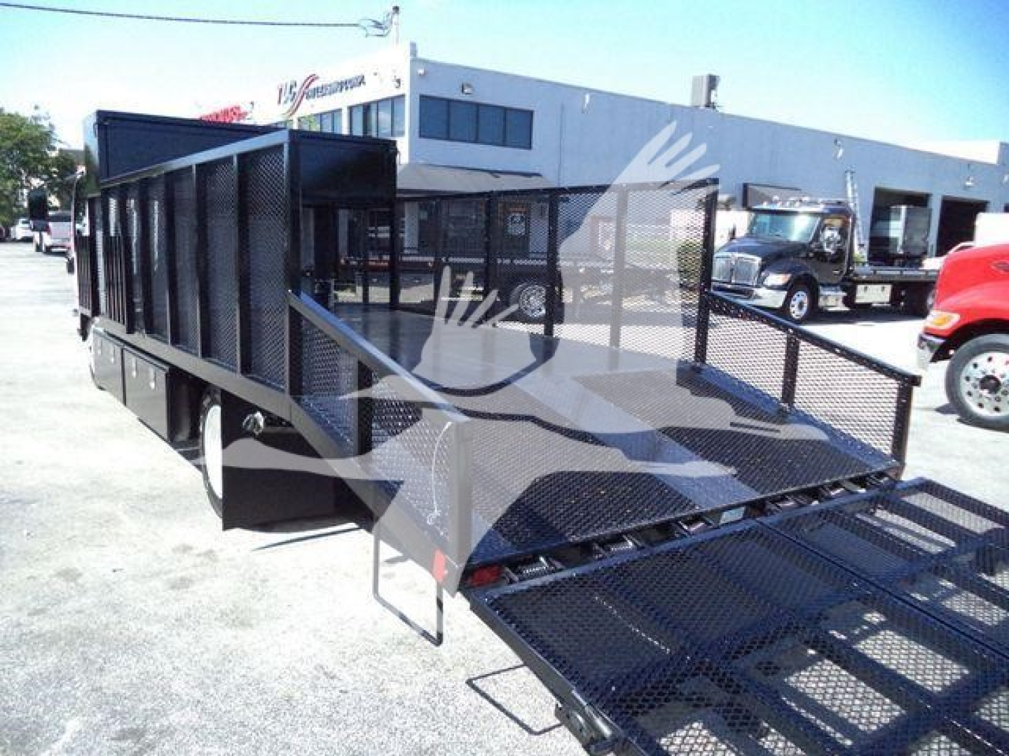 Isuzu NPRHD landscape truck with a long open flatbed trailer and side rails, viewed from front left, showing metal ramp gate.